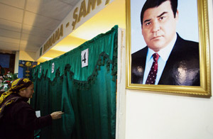 Volička vchází za plentu ve volební místnosti v Turkmenistánu, ze zdi vlevo na ni z portrétu shlíží zesnulý prezident 